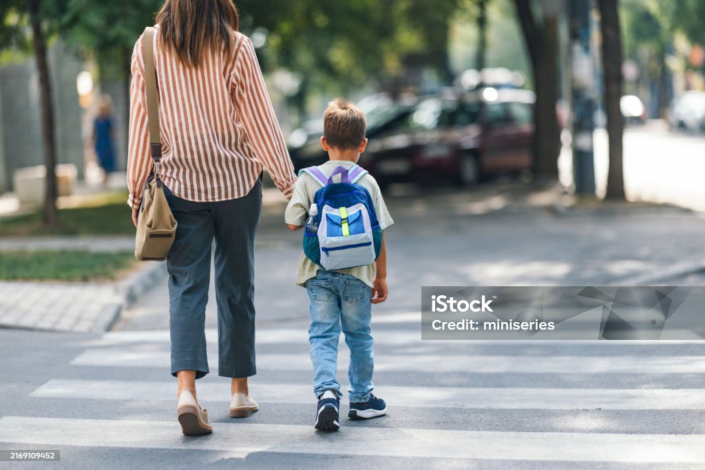 A mother and her young son holding hands while walking to school. The boy carries a backpack, symbolizing the start of a new educational journey.